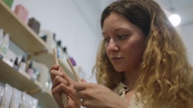 Kızıl saçlı kadın doğal ahşaptan yapılmış organik diş fırçasını seçiyor. Kıvırcık saçlı kadın müşteri süpermarketten eko ürünler alıyor.