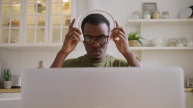 Afro-Amerikalı öğrenci kulaklık takıp laptoptaki ses derslerini dinliyor. Gözlüklü adam mutfakta tezgaha yaslanır. Yavaş çekimde yakın çekim.