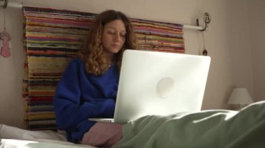 Serbest programcı konsantre kadın evde, yatakta battaniyenin altında, çevrimiçi eğitim, uzaktan çalışma altında bilgisayar başında çalışıyor.