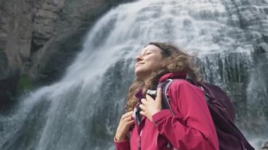 Seyahat ederken özgürlük ve macera hissi. Pembe zarlı ceketli, sırt çantalı bir turist kadın göğsüyle derin derin nefes alıyor ve dev bir arka planda temiz havanın tadını çıkarıyor.