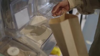 Paketlemeden alışveriş yapan bir kadın, bir kepçe dolusu beyaz buğday ununun içine yakın çekimden bir kepçe koyar. Ağırlık atölyesinden çevre dostu self-servis, sıfır atık