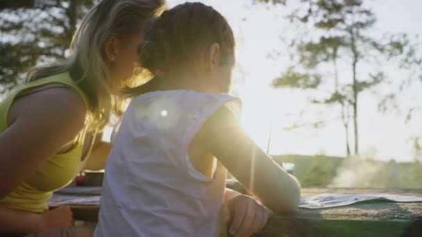 在大自然的家教中 年轻的母亲带着女儿在湖畔的森林里画画 在夕阳西下的阳光下 在新鲜的空气中免费接受教育 — 图库视频影像