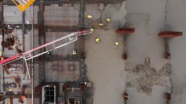 İnşaat alanında beton döken koruyucu miğferli işçilere tepeden bakılıyor. Çok katlı bir binanın ya da alışveriş merkezinin monolitik yapısı.