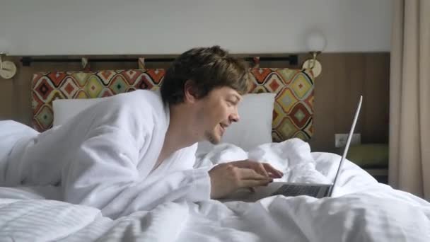 Szczęśliwy Radosny Człowiek Skaczący Łóżku Wpisujący Tekst Laptopie Białym Płaszczu — Wideo stockowe