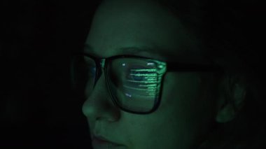Kadın hacker, bir bilgisayar ekranından program kodunun yansıması olan karanlık çekimde verileri analiz eder, siyah bir ekrandaki sistemi ve veri güvenliğini hackler.