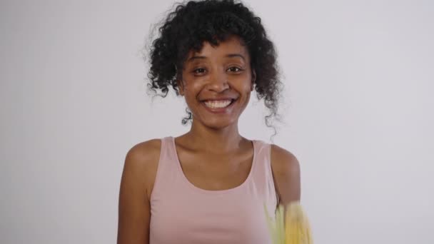 一个身材矮小的混血快乐女人的肖像手里拿着玉米芯 有机产品对健康有益 健康的蔬菜 穿着背心的快乐卷曲的女人愿意选择Gmo — 图库视频影像