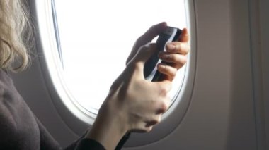 Kadın, bir uçağın arka planında otururken elinde bir cep telefonu tutuyor. Yakın plan, sosyal ağlarda internet iletişimi. Aerofobi, bir kız stresle başa çıkabilir.