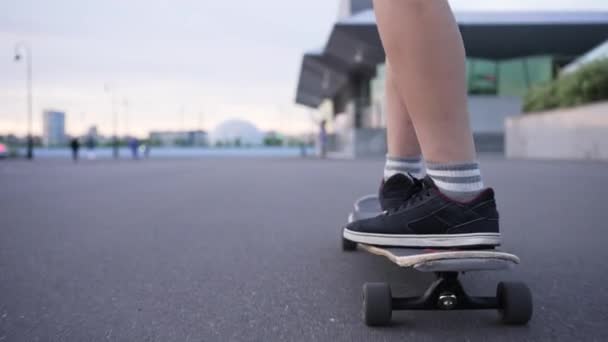 穿着黑色运动鞋的少女在一块长木板上跳舞 转弯360度 绕着她的轴 紧闭着她的腿 在这个城市 女学生骑的是平顺的柏油 — 图库视频影像