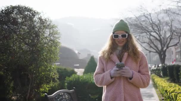 Stylowa Kobieta Okularach Przeciwsłonecznych Różowym Futrze Powoli Przechodzi Przez Park — Wideo stockowe