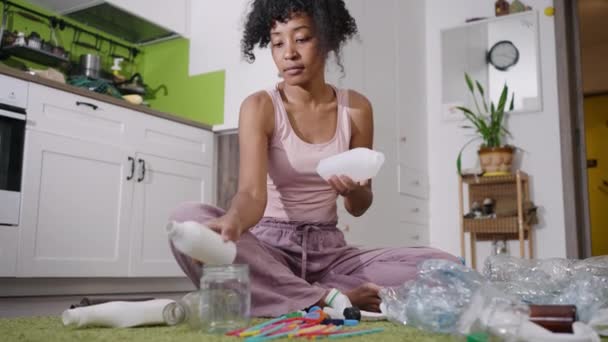 一个漂亮的女人坐在地毯上整理垃圾 整理不同类型的塑料和玻璃瓶 循环利用和保护环境的概念 — 图库视频影像