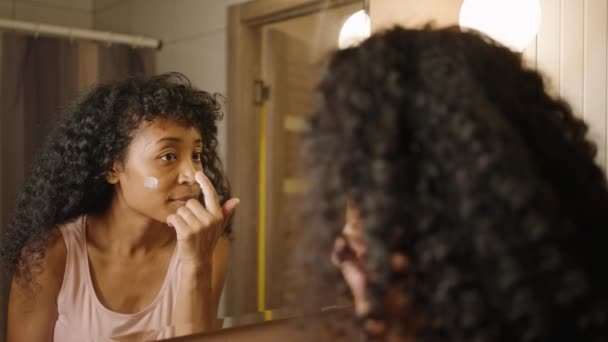 Mulher Biracial Aplica Hidratante Seu Rosto Banheiro Frente Espelho Cuidados — Vídeo de Stock