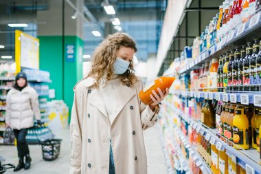 Genç bayan müşteri bir süpermarkette kabak havucu suyu etiketinin üzerindeki kompozisyonu dikkatle okuyor. Uygun beslenme kavramı ve katkı maddeleri olmadan kaliteli ürünlerin seçimi ve
