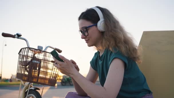 Mujer Joven Gafas Auriculares Con Una Bicicleta Utiliza Teléfono Inteligente — Vídeo de stock