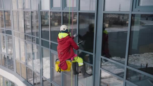 玻璃垫圈攀登者用钢丝绳 防护头盔和安全带擦拭房子正面的阳台玻璃 一个快乐的人正在做他最喜欢的工作 一个极端的职业 — 图库视频影像
