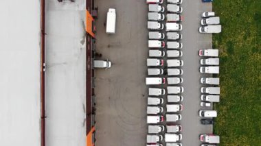 Park halindeki kamyonların kaldırımlı bir otoparkta düz sırada durduğu bir lojistik deposunun tepeden aşağı manzarası.