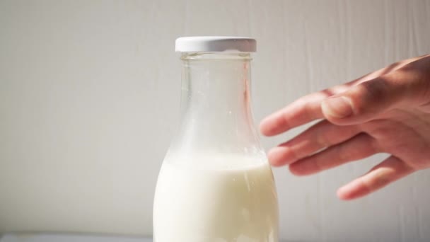一个女人的手在白墙的后面拿着一个装有牛奶的玻璃瓶 里面有阳光 — 图库视频影像