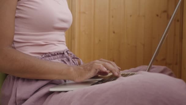 在家里阳台上的笔记本电脑上工作的混血女自由职业者 没有脑袋的远程工作者 穿着粉色睡衣坐在地板上的设计师 自由时间安排 — 图库视频影像
