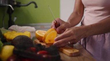 Kadın elleri taze, sulu bir portakalı tahta bir tahtanın üzerinde mutfakta dilimlere ayırdı. Akşam yemeği için evde meyve kesen melez bir kadın, sağlıklı beslenme konsepti.