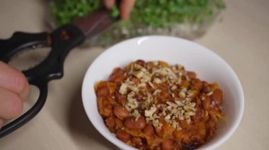 Kadın elleri mutfak makası ile filizlenmiş mikroyeşillikleri keser ve masadaki güzel ve vitamin açısından zengin tabağa ekler. Vejetaryen fasulye yemeği.