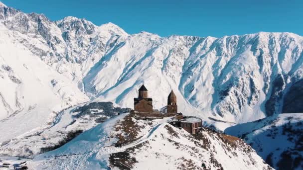 在高高的雪山的背景下 绕着一座古老的石头基督教教堂飞行 冬季山脉和历史宗教建筑的壮丽全景 — 图库视频影像