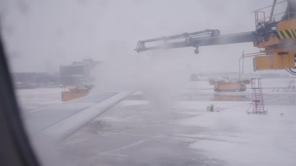 在机场用防冻液处理机翼 从窗户往外看 工人将液体喷到飞机表面以保证飞行安全 — 图库视频影像