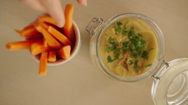 Mano Las Mujeres Toma Palo Zanahoria Sumerge Hummus Con Hierbas — Vídeos de Stock