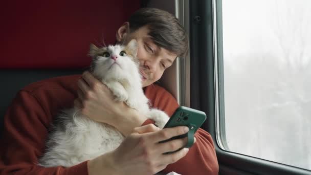 Radosny Człowiek Patrzy Zdjęcia Telefonie Przytulając Kota Pociągu Podróżowanie Zwierzątkiem — Wideo stockowe