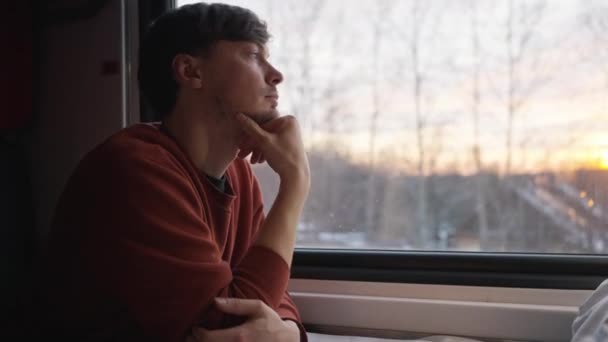 若い男が列車で旅行し 冬の森が窓の外で明るく見える — ストック動画