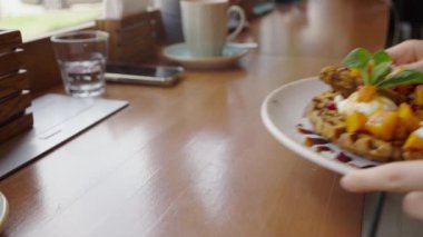 Kadın, pencerenin karşısındaki bir kafede böğürtlen ve ballı vejetaryen Viyana waffle 'larını masaya koyar. Lezzetli ve sağlıklı kahvaltı.