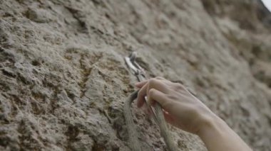 Bir kadının eli tırmanma halatını sıkıca bir kayanın tepesindeki güvenlik elemanına geçirir. Dağlara tırmanır, açık hava sporu yapar.