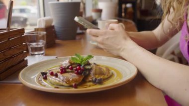 Kadın kahvaltıda elinde akıllı telefonuyla pencerenin yanındaki kafede oturuyor. Yanında gözleme ve yakın çekim var. İş kadını bir kafede cep telefonuyla iletişim kuruyor..