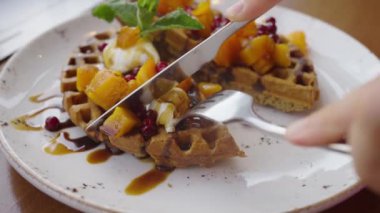 Kadınların elleri, iştah açıcı vejetaryen waffleları balkabağı ve balla kesiyor. Bıçak ve çatalla yakın plan. Vejetaryen bir kafede sağlıklı ve lezzetli yemekler..