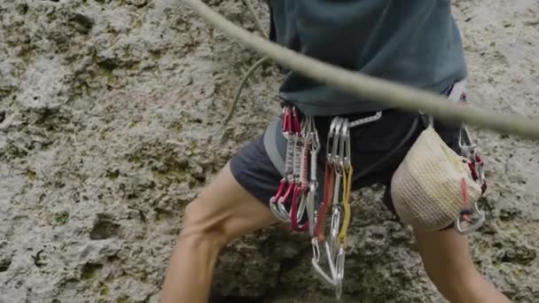 クライマーは岩面の上に達し 登るのに必要な激しい焦点を強調しています 男性のクライマーは岩の上のカラビナーにロープをスナップし 保険を組織します — ストック動画
