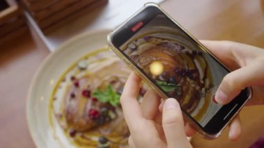 Kafedeki bir kadın, telefon kamerasında naneli, böğürtlenli ve böğürtlenli vejetaryen pirinç kreplerini vuruyor. Sosyal ağlar için yemek videosu kahvaltısı.