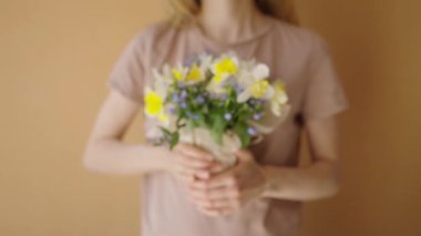 Tanımlanamayan bir kadın bir buket nergis çiçeğini, el işi kağıda sarıp bej bir duvara doğru çeker.