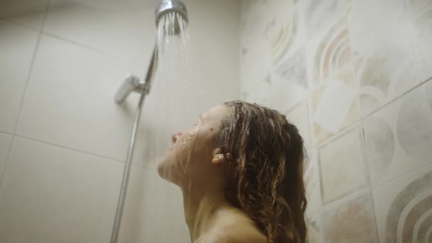 一个女人紧闭双眼站在温暖的水流下 享受着洗浴 按摩头和放松 年轻女子在瓷砖浴室享受轻松淋浴的乐趣 — 图库视频影像