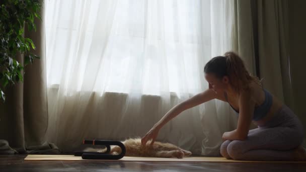 在一个阳光灿烂的房间里 当一个女人在瑜伽垫上向她那只顽皮的猫伸出手来 象征着和平与友谊时 那是一个宁静的时刻 这个女人从训练中抽出一点时间和心爱的宠物猫玩耍 — 图库视频影像