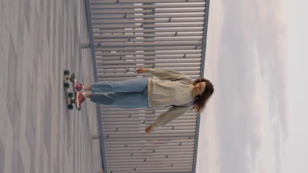 年轻无忧无虑的女人骑着滑板沿着长廊 垂直的视频 时髦的姑娘背着背包坐在长板上 — 图库视频影像
