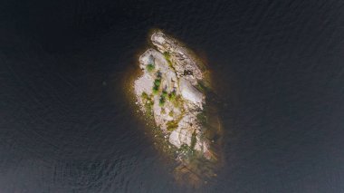 Yukarıdan, seyrek bitki örtüsüne sahip ıssız bir kayalık ada karanlık ve dalgalı sulara karşı duruyor. Uçsuz bucaksız bir zıtlık ve yalnızlık hissi yaratıyor..
