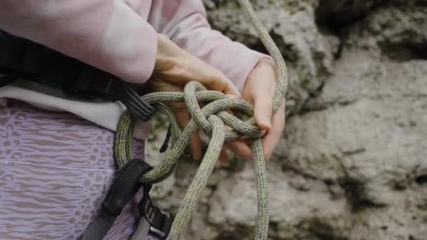 女性のロッククライマーは 急な崖に登る前に安全ハーネスに登るノットを結び 手を閉じます エクストリーム スポーツ — ストック動画