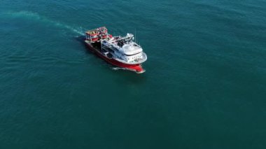 Küçük bir balıkçı teknesi sabah balığından sonra limana döner, hava manzaralı. Kırmızı bir gemi turkuaz bir denizde yelken açar. Güneşli bir havada dalgalarda sallanır..