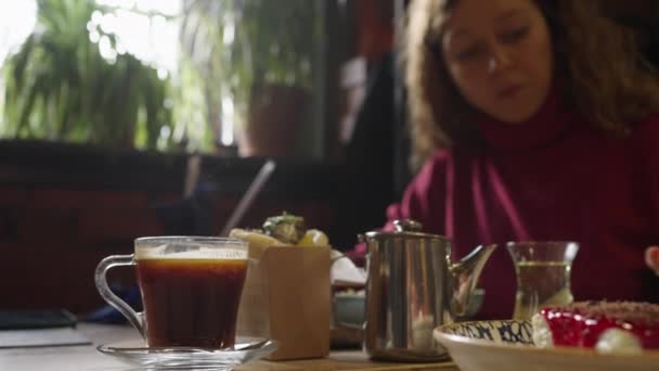 ウィンドウの近くに座っているレストランで昼食をとっている女性は ビデオが焦点を当てていない 彼女はパンのトルティーヤのスライスにソースを広げる 蒸気はコーヒーのカップから上昇する — ストック動画