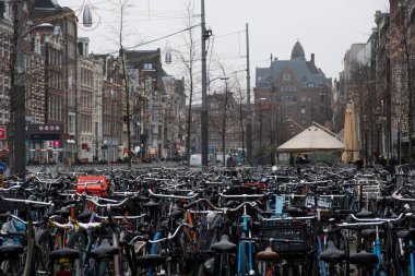 Amsterdam Bisiklet Otoparkı aşırı yüklendi. Park halindeki bisikletlerden oluşan yoğun bir deniz ön plana hakim olurken, Amsterdam 'ın klasik mimarisi ve şehir hayatı arka planda bulanıklaşıyor. Hollanda, Amsterdam, Ocak