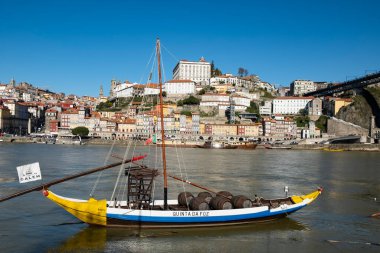 Geleneksel olarak şarap fıçılarını taşımak için kullanılan renkli bir Rabelo teknesi Portos tarihi şehir manzarasına karşı Douro Nehri 'nde yüzer. Portekiz, Porto, Ocak 2020.