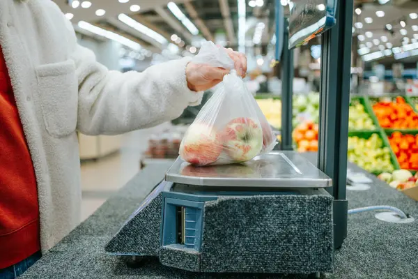 Süpermarketin Üretim Bölümü 'nde İnsan Ağırlığı Elmaları' nın Yakın Çekimi. Alışverişçilerin elleri bir torba taze elmayı dijital ölçekte tartarak üretim bölümünde satın alınabilecek en uygun miktarı sağlar.