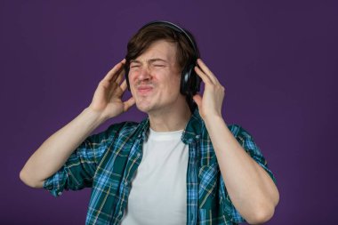 Genç bir adam, mor bir arka planda izole bir şekilde kulaklıklarıyla çalan müziğe kendini kaptırdığı için sevinçten ürker. Müzik Coşkusu Sesin içinde Kaybolmak