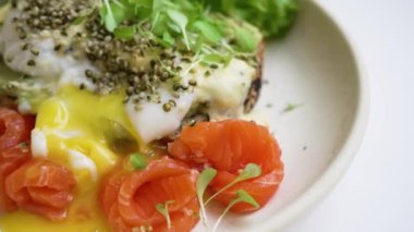 Gurme Somon ve Avokado tostu. Yumuşak haşlanmış yumurta ve füme somonla kaplı, lezzetli bir brunch deneyimi için taze otlar ve tohumlarla süslenmiş iştah açıcı avokado tostu..