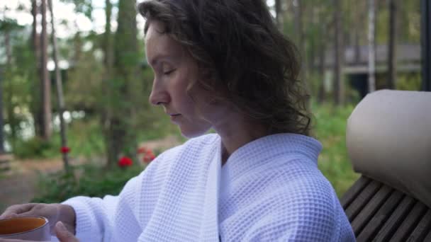 Расслабленная Женщина Пьет Успокаивающий Травяной Чай Сидя Кресле Лесной Террасе — стоковое видео