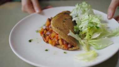 Fasulye ve doğranmış sebze karışımı ile dolu sağlıklı bir pita cebi, besleyici bir yemeği ön plana çıkaran beyaz bir tabakta taze yeşil bir salata ile eşleştirilir. Sağlıklı ve lezzetli bir vegan yemeği..