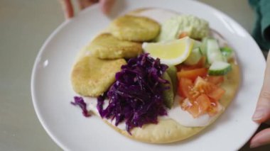 Taze bir vejetaryen yemeği, içinde altın patates köfteleri, yassı ekmeğin üzerine keskin bir sos serpilmiş ve yanında çıtır sebzeler bulunan, tadını çıkarmaya hazır. Kadın elleri yavaşça lezzetli vejetaryen yemeklerini çeviriyor.